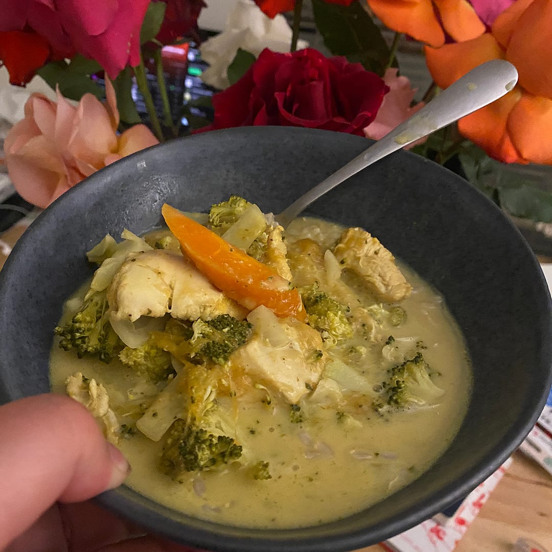 chicken mango curry in blue ceramic bowl with various colours of rose flowers behind