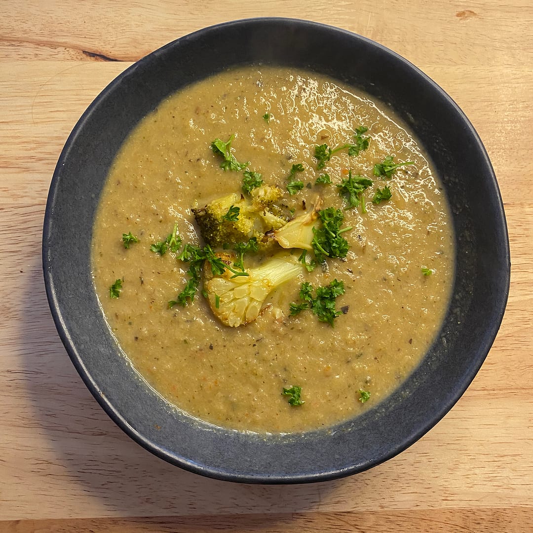 creamy roasted vegetable soup - a bowl of soup garnished with cauliflower and broccoli florets and parsley in a blue bowl on a wooden table